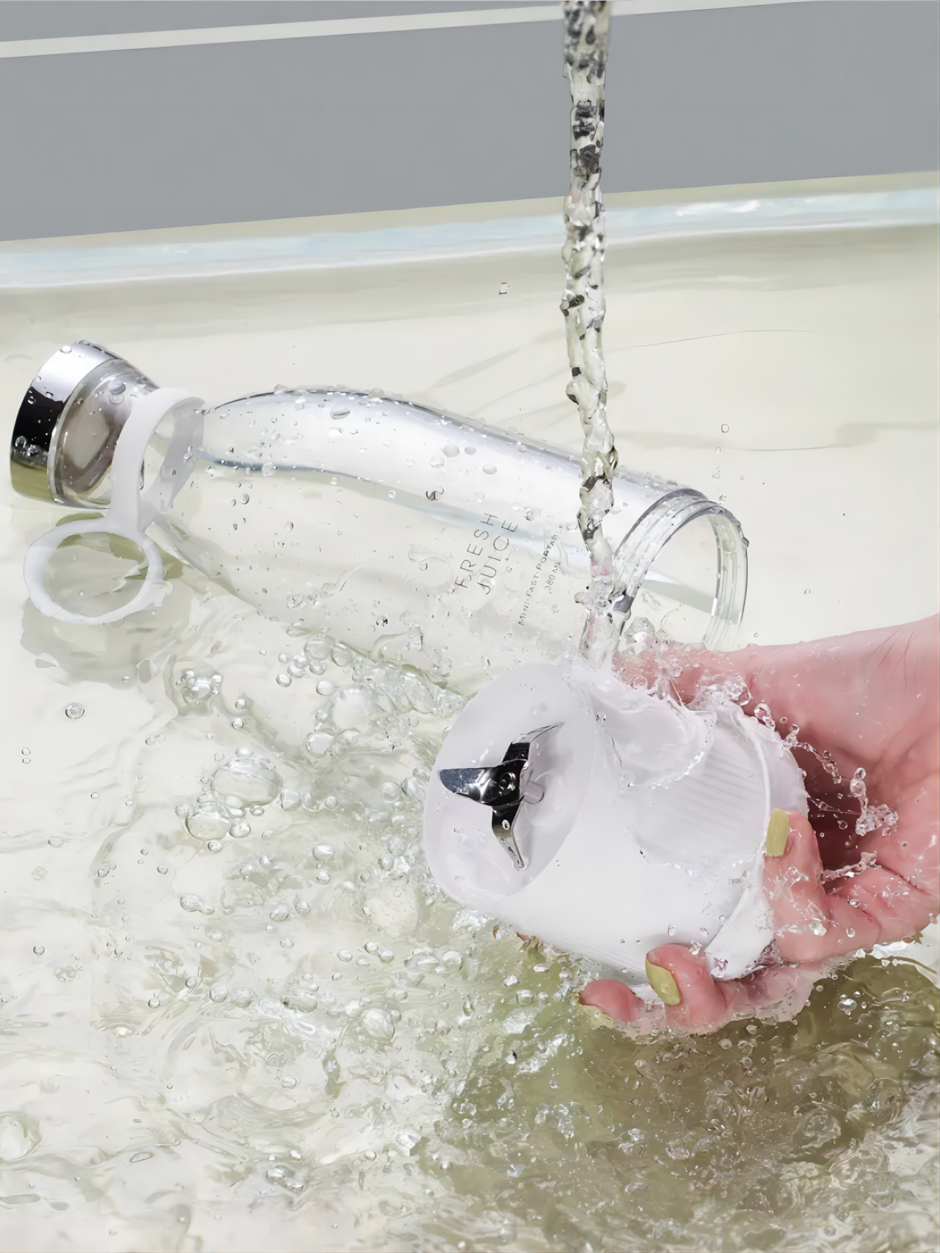 Clear water bottle being rinsed under running water with a hand holding it.