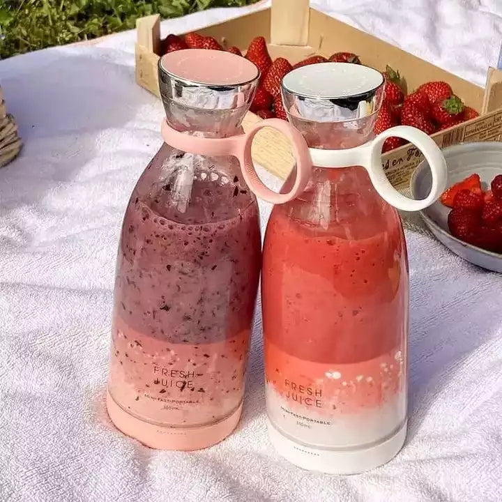 Two glass bottles with pink and red drinks on a white blanket with strawberries in the background.